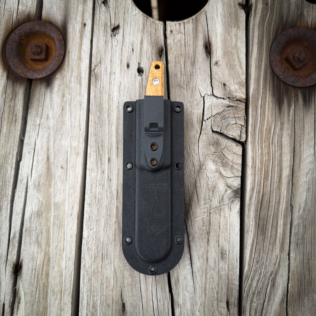 Knife in a think kydex pocket sheath. Resting on rustic wooden surface