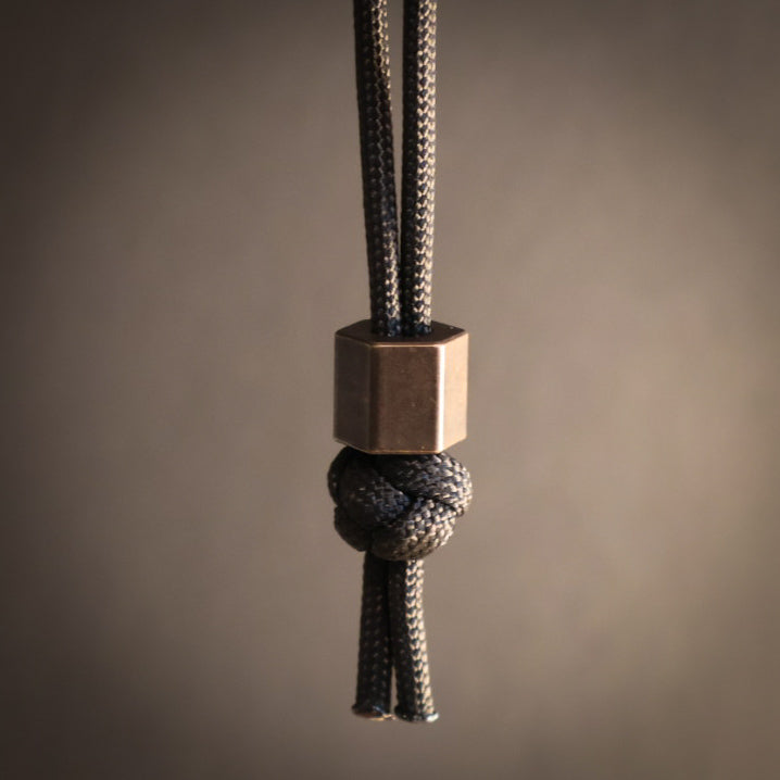 Close-up of a braided rope with a hexagonal metal bead on a brown background