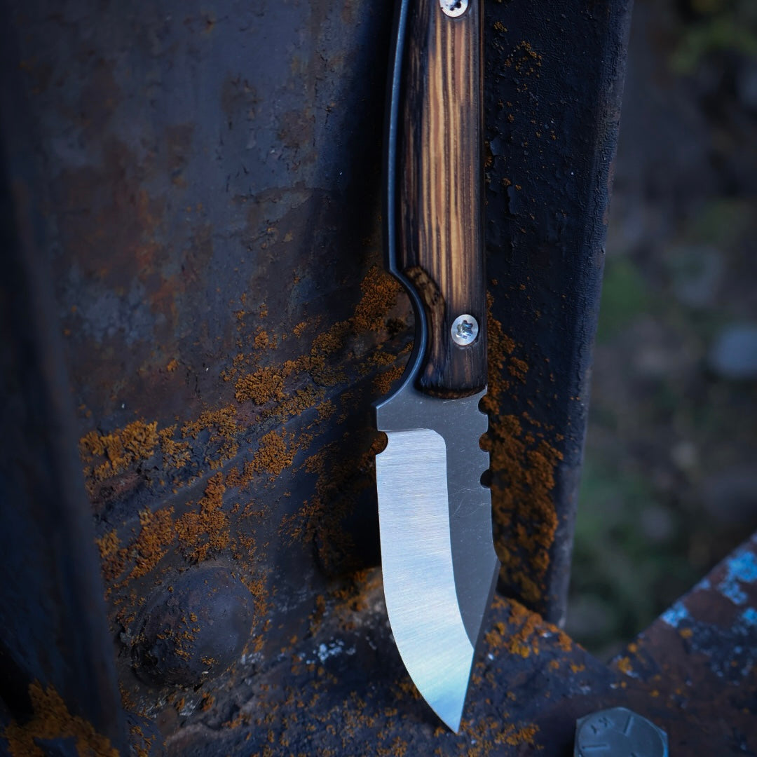 knife with satin blade and rustic wooden handles leaning up on rusted metal surface
