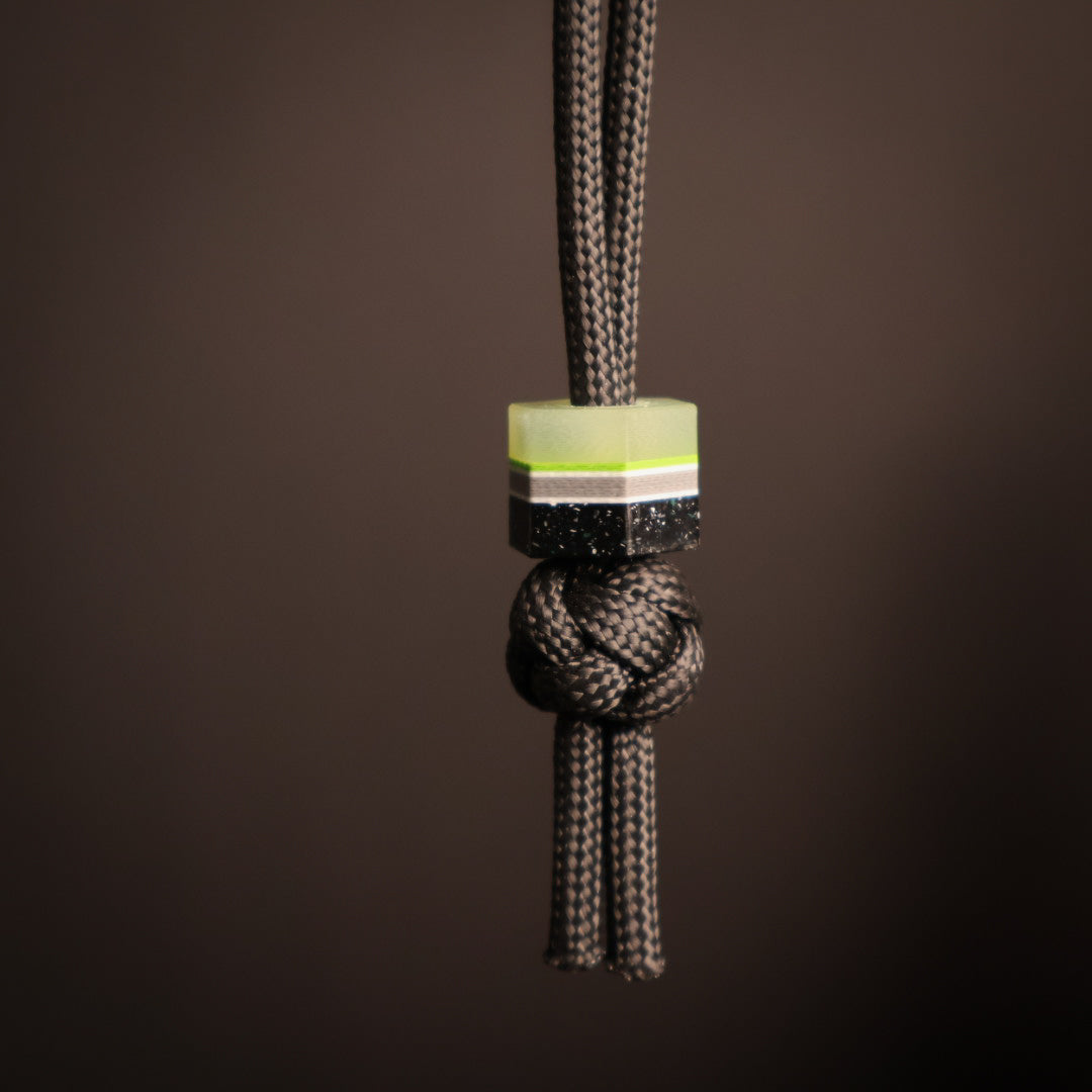 Hexagonal lanyard bead with green, gray, white, and black layers. Hanging on black paracord lanyard