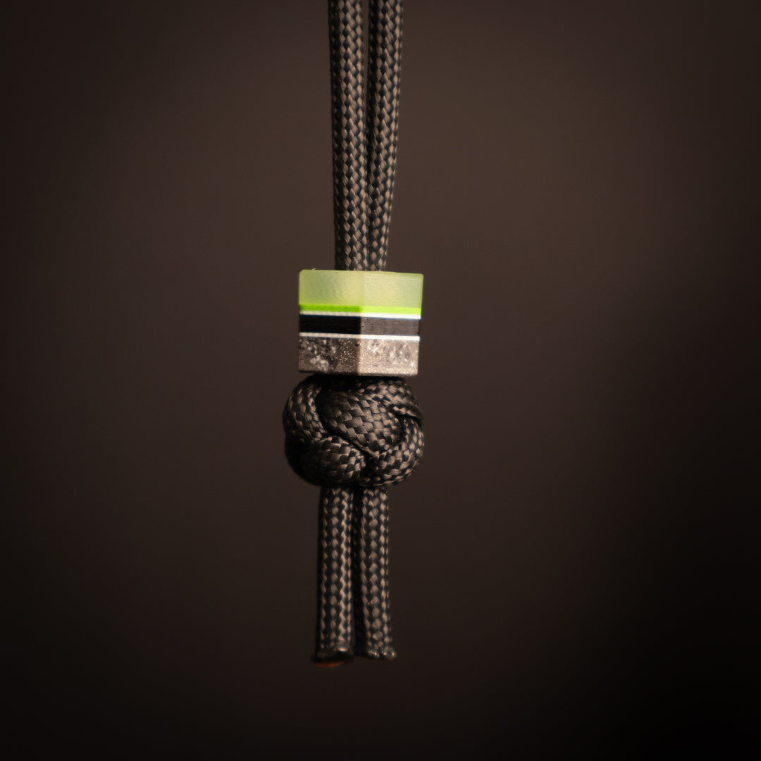 Hexagonal lanyard bead with green, gray, white, and black layers. Hanging on black paracord lanyard