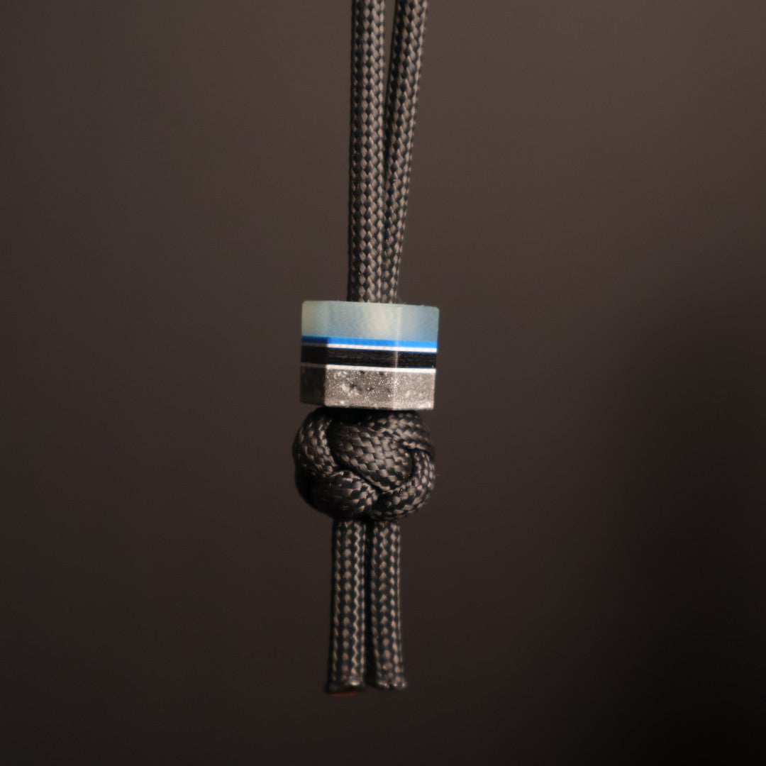 Hexagonal lanyard bead with blue, gray, white, and black layers. Hanging on black paracord lanyard