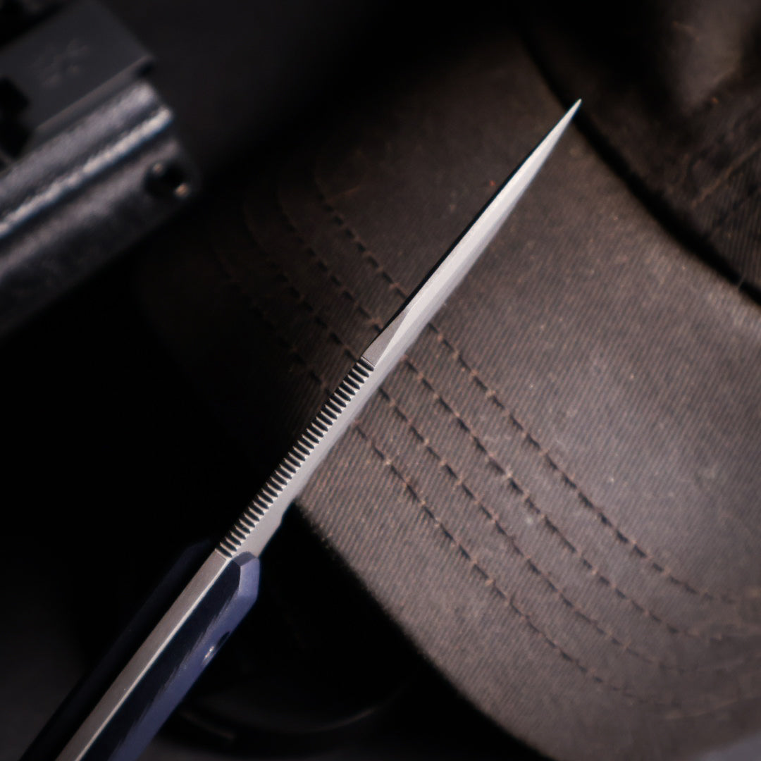 close up of fine jimping on the spine of a knife that is leaning against black ballcap
