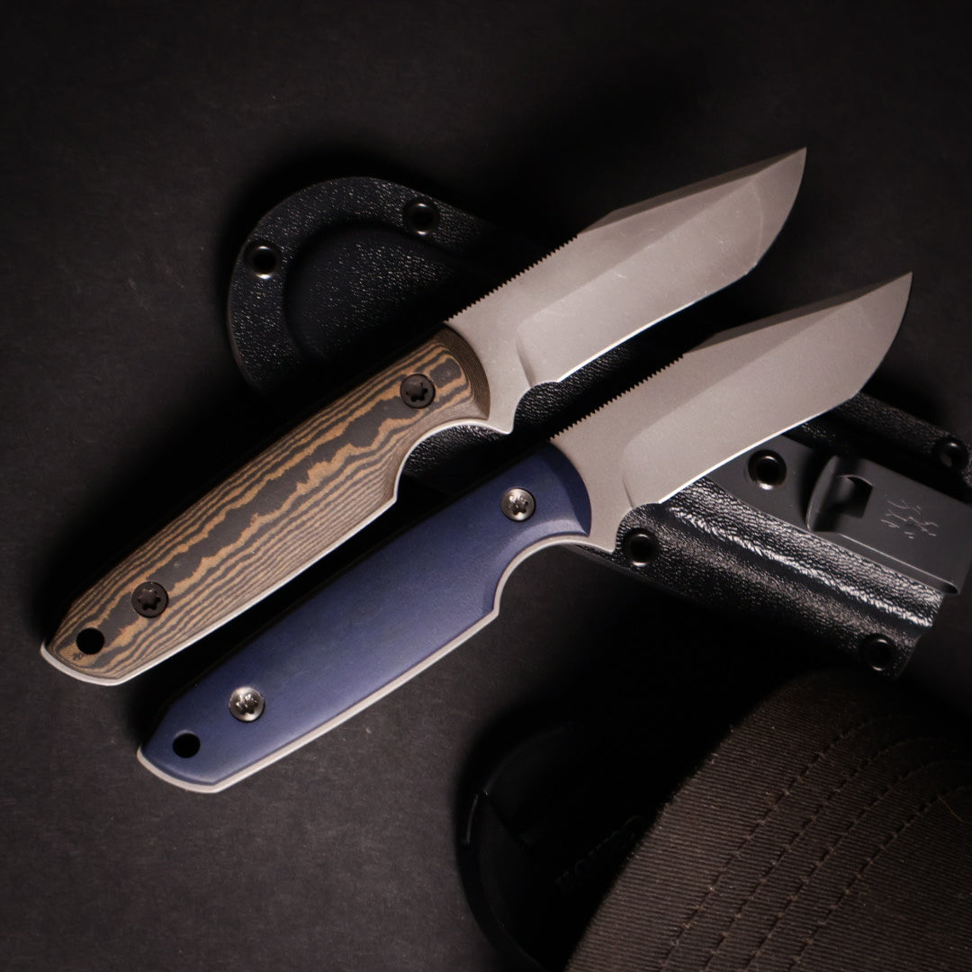 two fixed blade knives resting on a kydex sheath with a black background