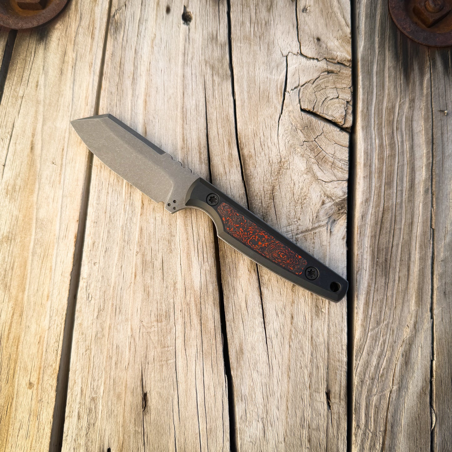 A fixed-blade knife with a matte gray blade and a black handle featuring a grey and orange inlay, resting diagonally on a rustic wooden plank surface.