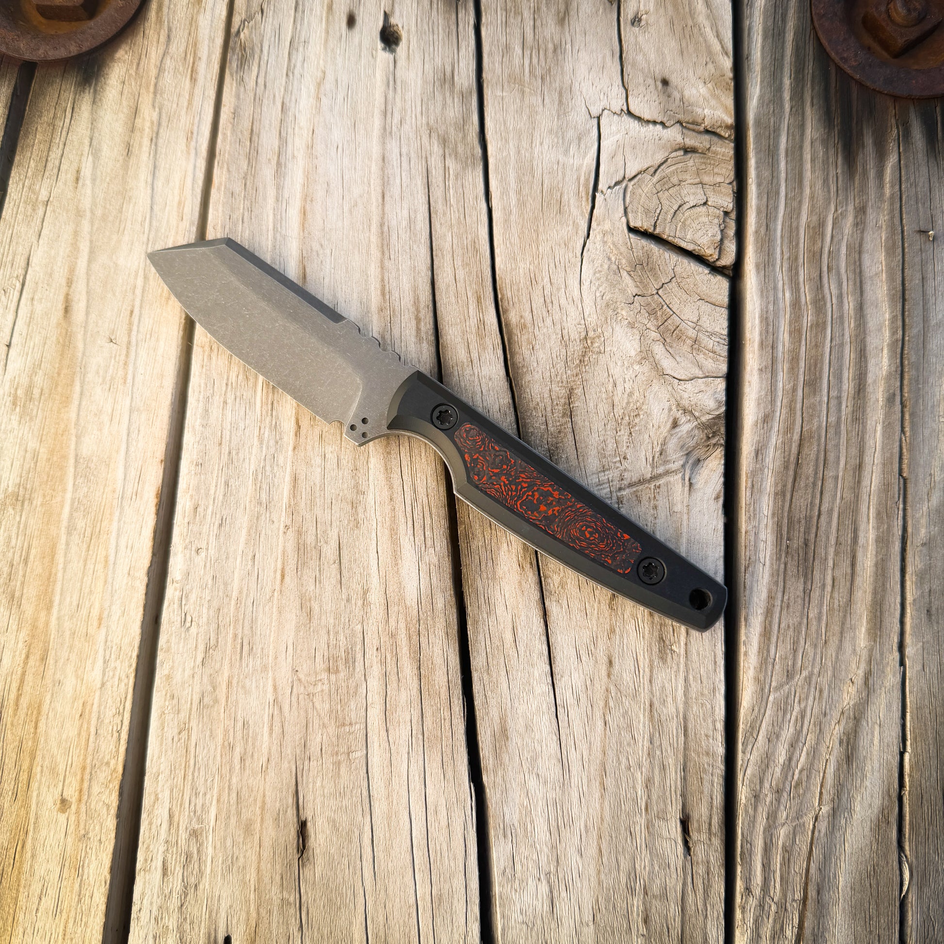 A fixed-blade knife with a matte gray blade and a black handle featuring a grey and orange inlay, resting diagonally on a rustic wooden plank surface.