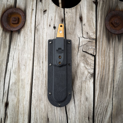 Knife in a think kydex pocket sheath. Resting on rustic wooden surface