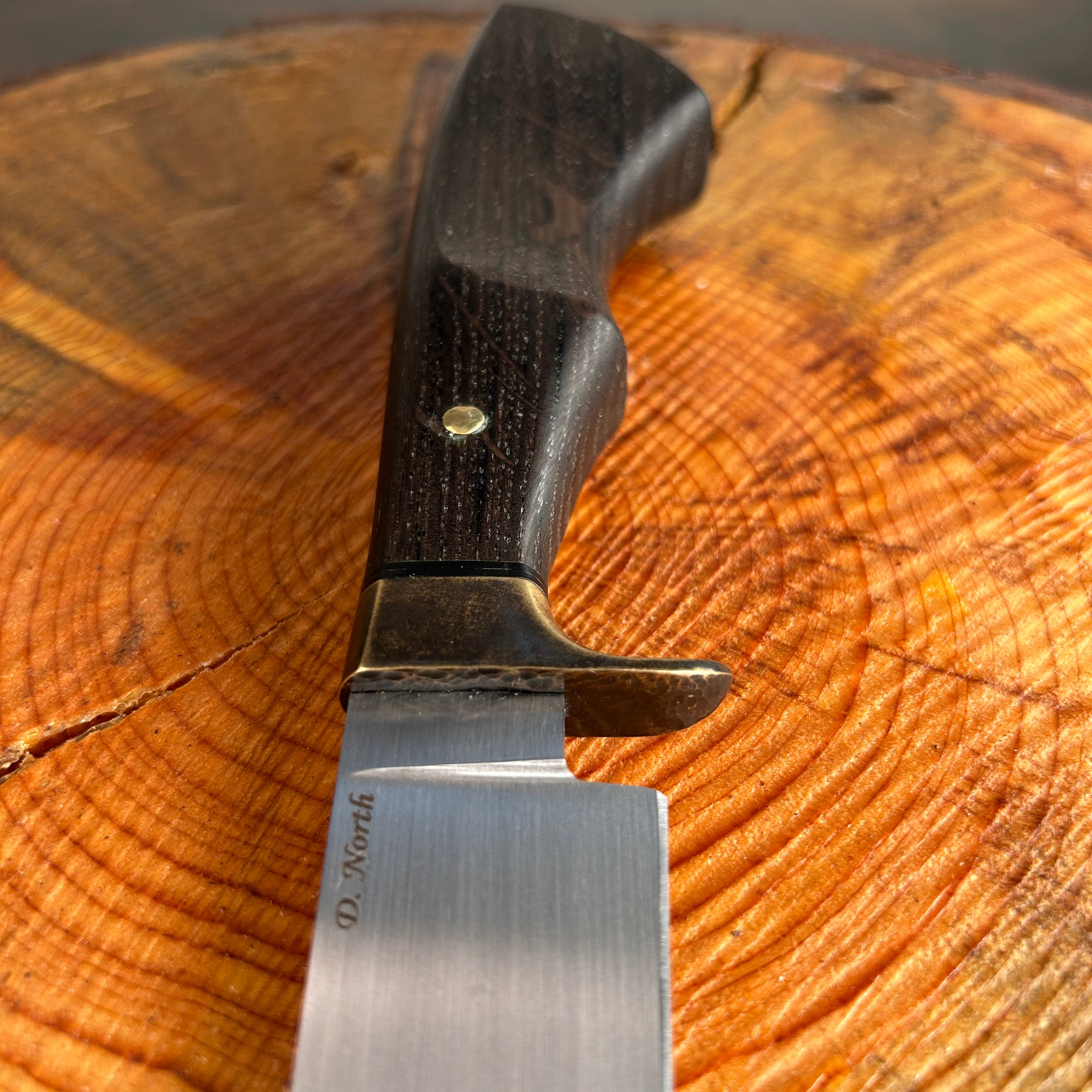 Knife handle with brass guard sitting on wooden stump