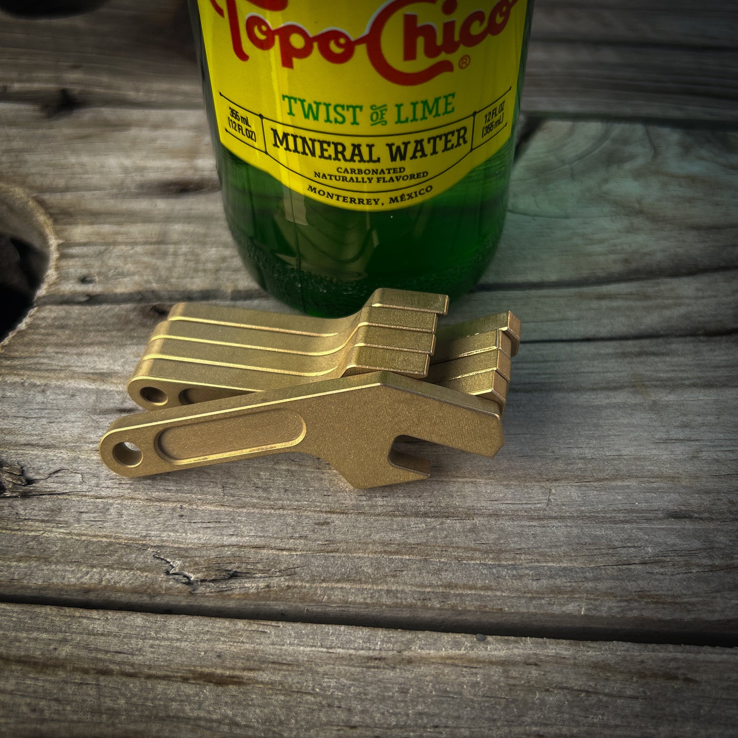 Brass keychain bottle openers sitting on wood surface next to glass bottle