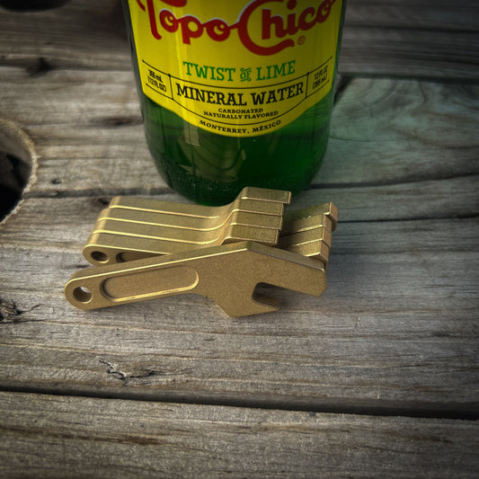 Brass keychain bottle openers sitting on wood surface next to glass bottle