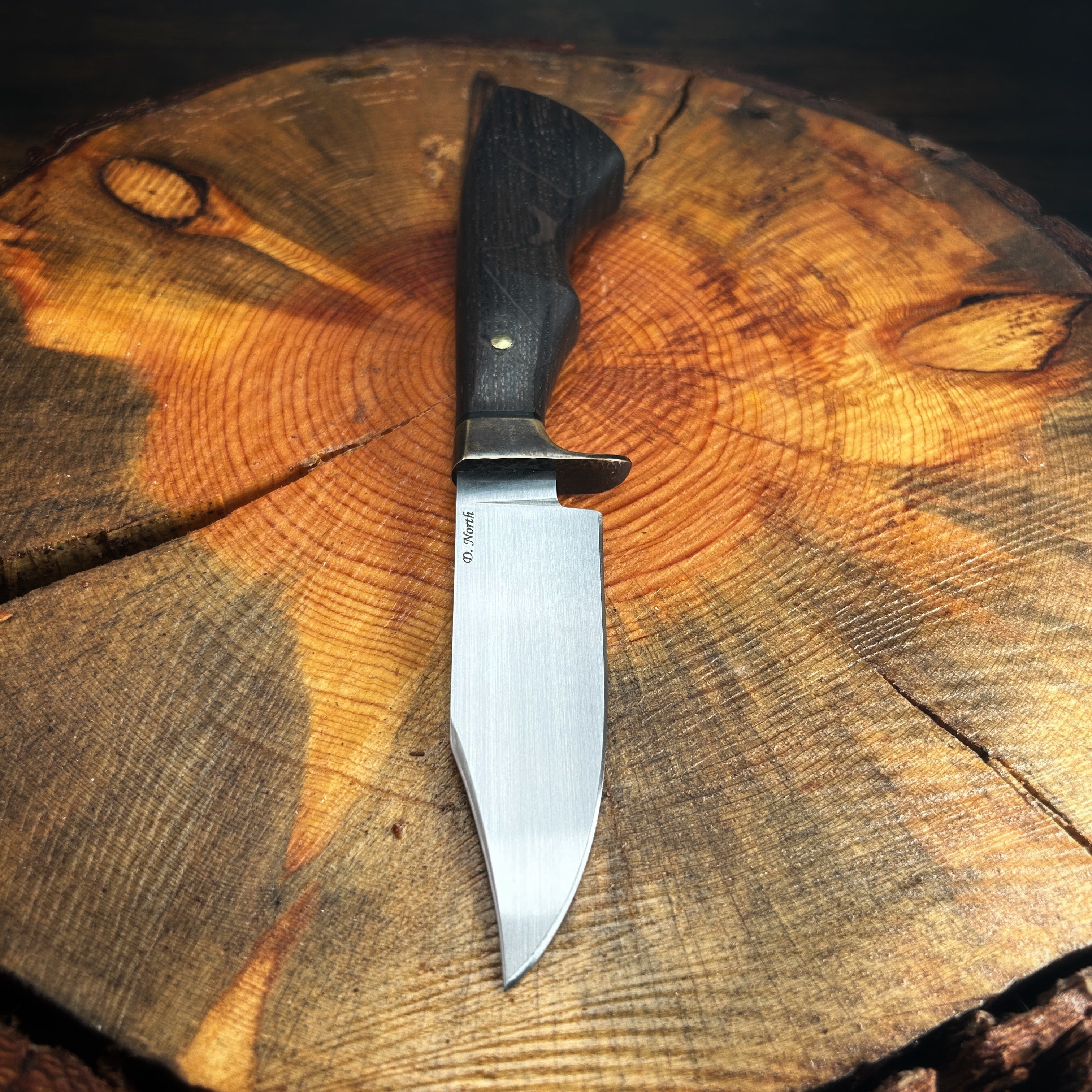 fixed blade knife with brass guard and bog oak handle sitting on pine stump