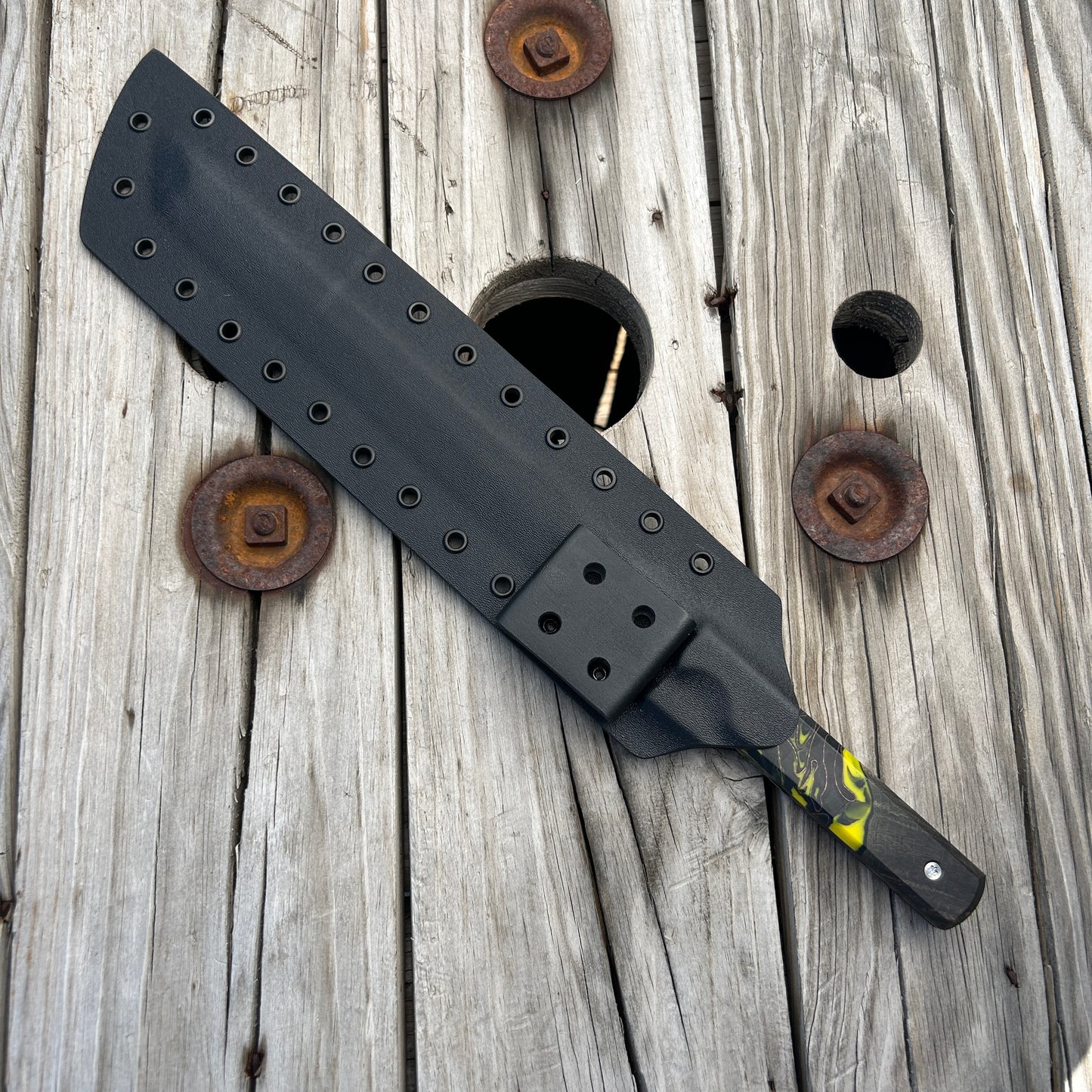 Black knife in sheath with a yellow handle on a wooden surface