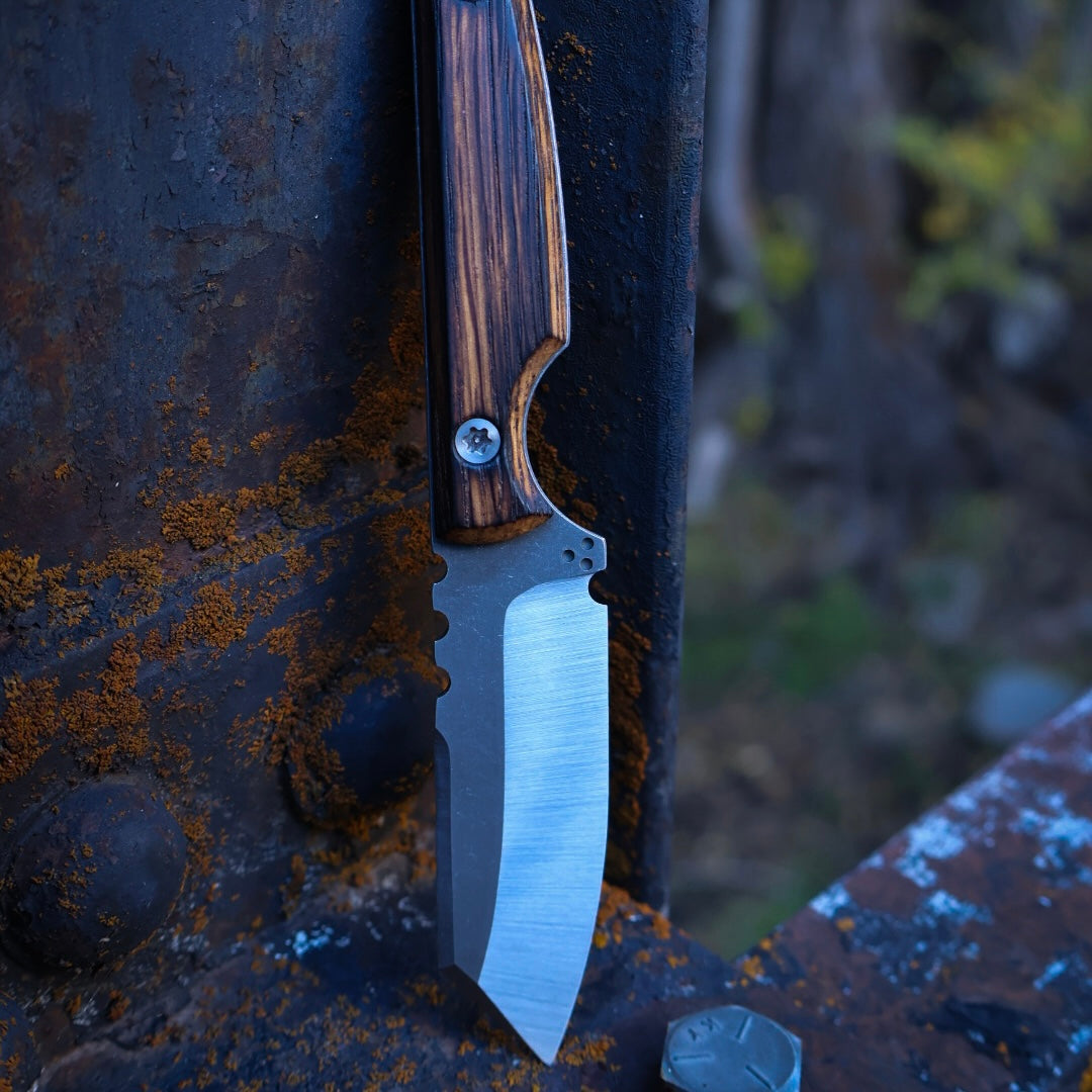 knife with satin blade and rustic wooden handles leaning up on rusted metal surface