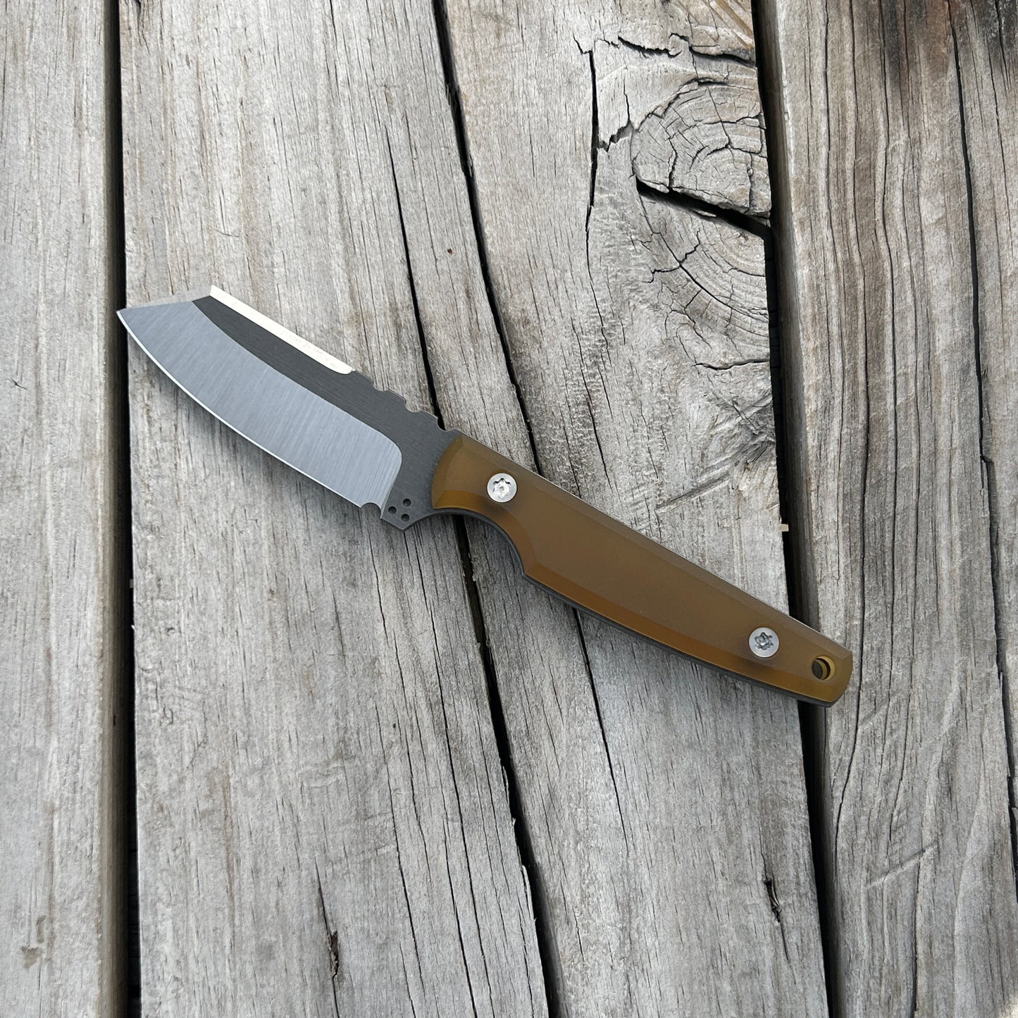 fixed blade knife with two tone blade and ultem handle sitting on wooden surface