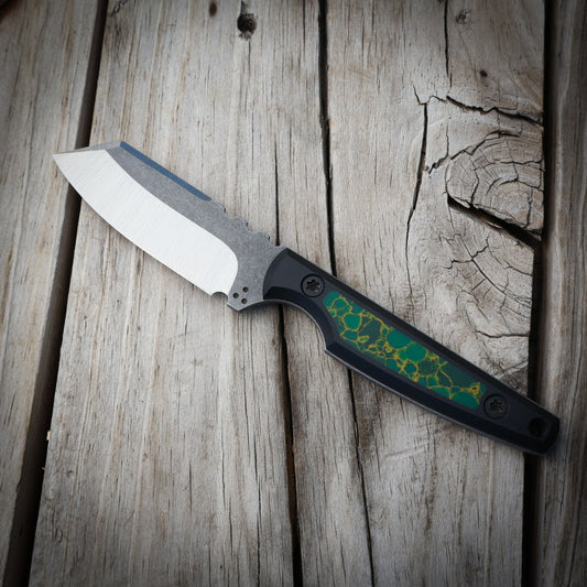 Knife with green decorative handle sitting on wooden surface 