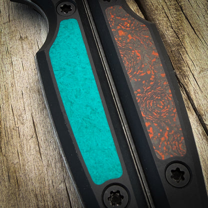Closeup of knife handle inlays. One is a bright teal green with shredded glass fibers visible within and the other is black, grey, and orange with a random pattern like topo or dunes. 