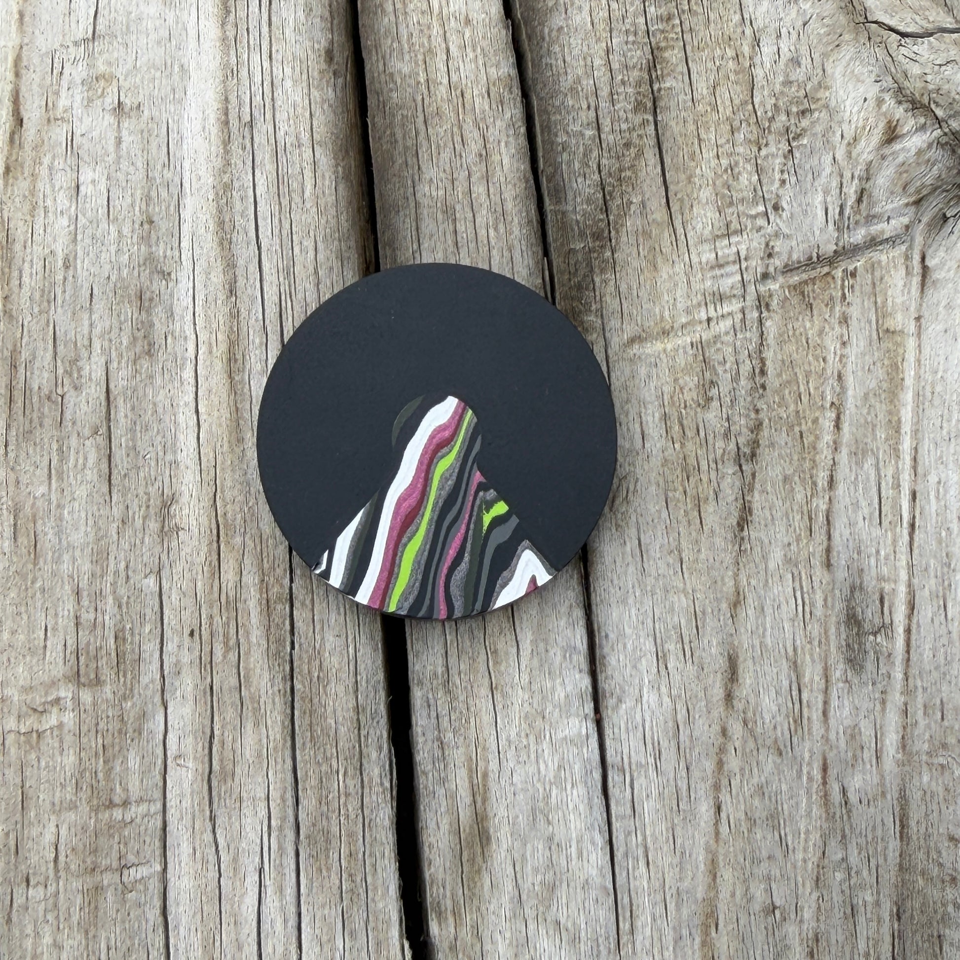 a round black coin with a triangular cutout with a colorful wedge inlay, laying on wooden surface 