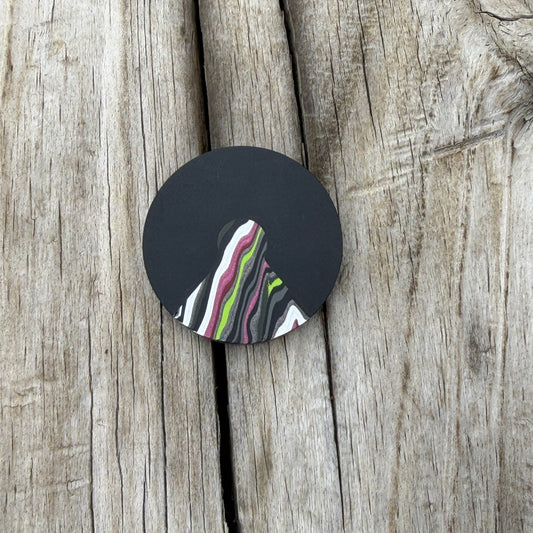 a round black coin with a triangular cutout with a colorful wedge inlay, laying on wooden surface 