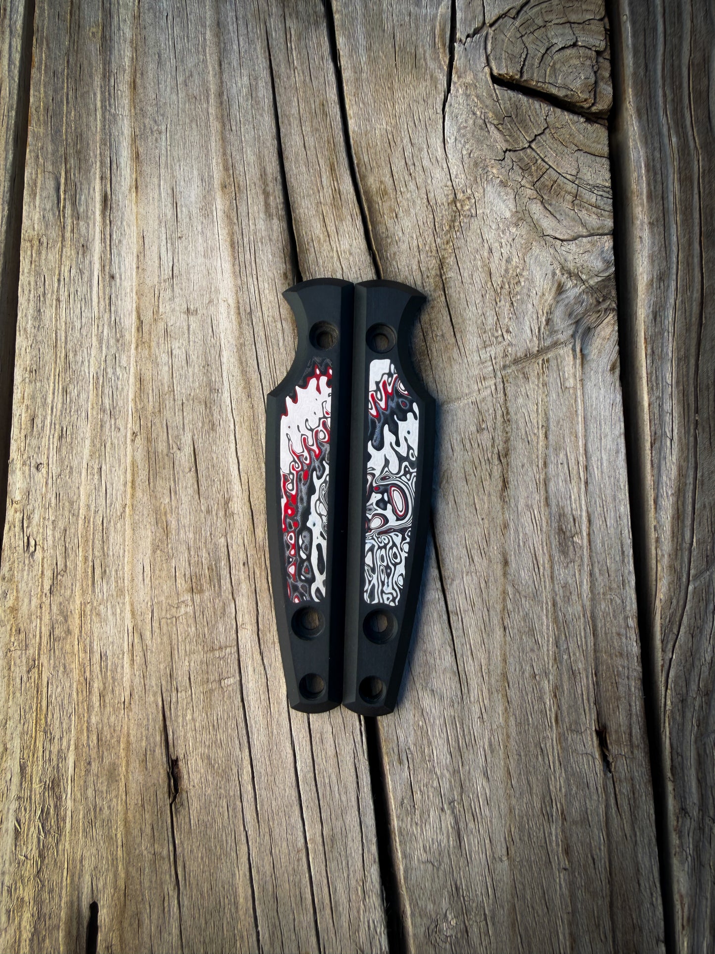 Black knife handle scales with colorful fordite inlays sitting on wooden surface 