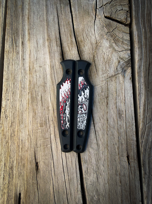 Black knife handle scales with colorful fordite inlays sitting on wooden surface 