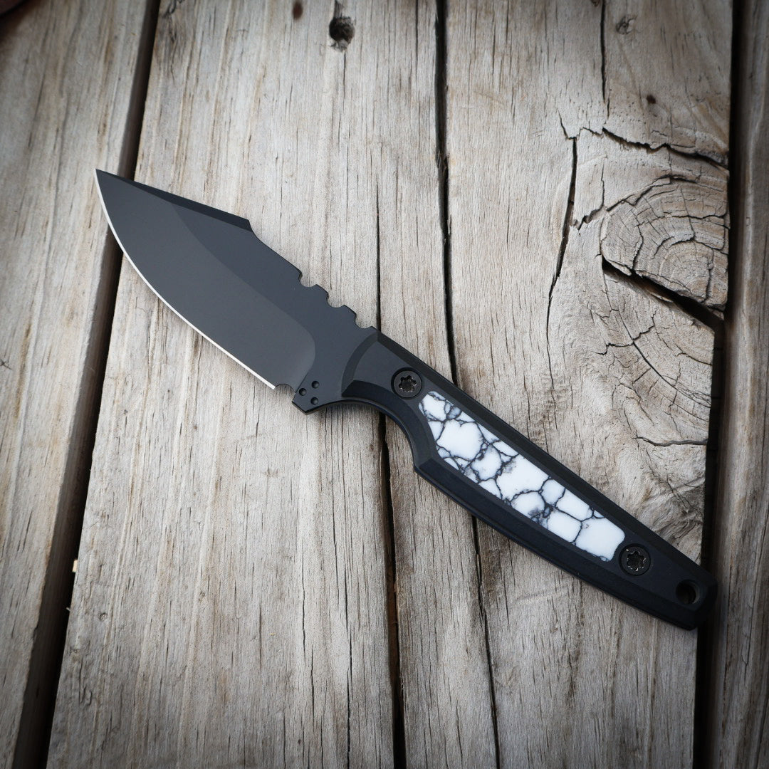 Fixed blade knife with black blade and white and black handle sitting on wooden surface