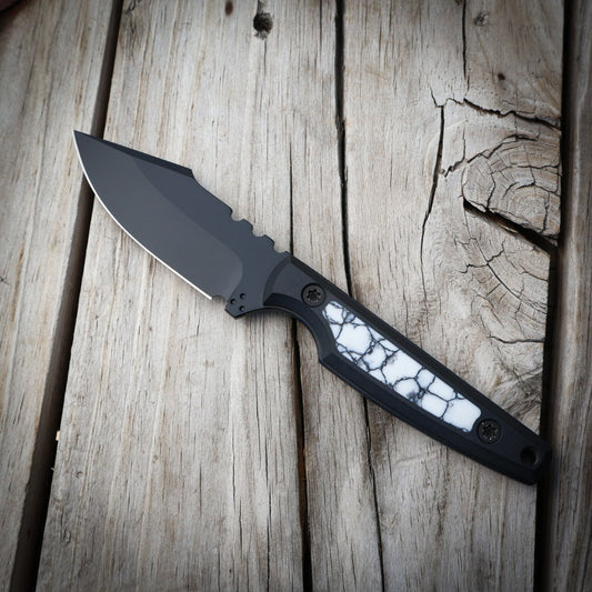 Fixed blade knife with black blade and white and black handle sitting on wooden surface