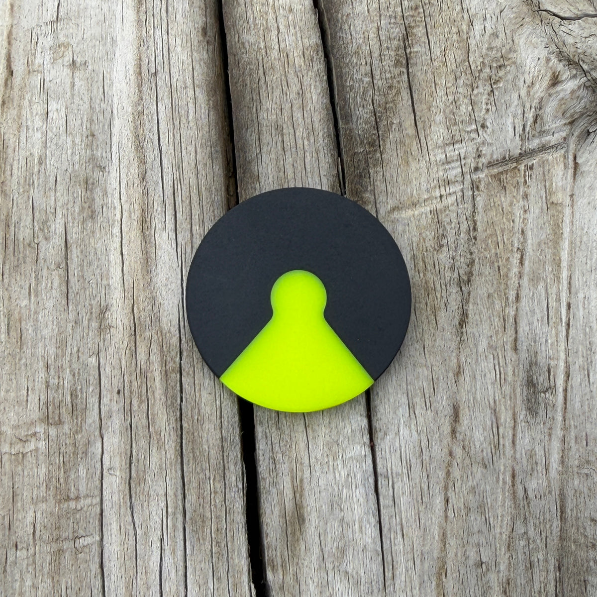 A circular black coin with a neon yellow keyhole design in the center, placed on a rustic gray wooden surface.