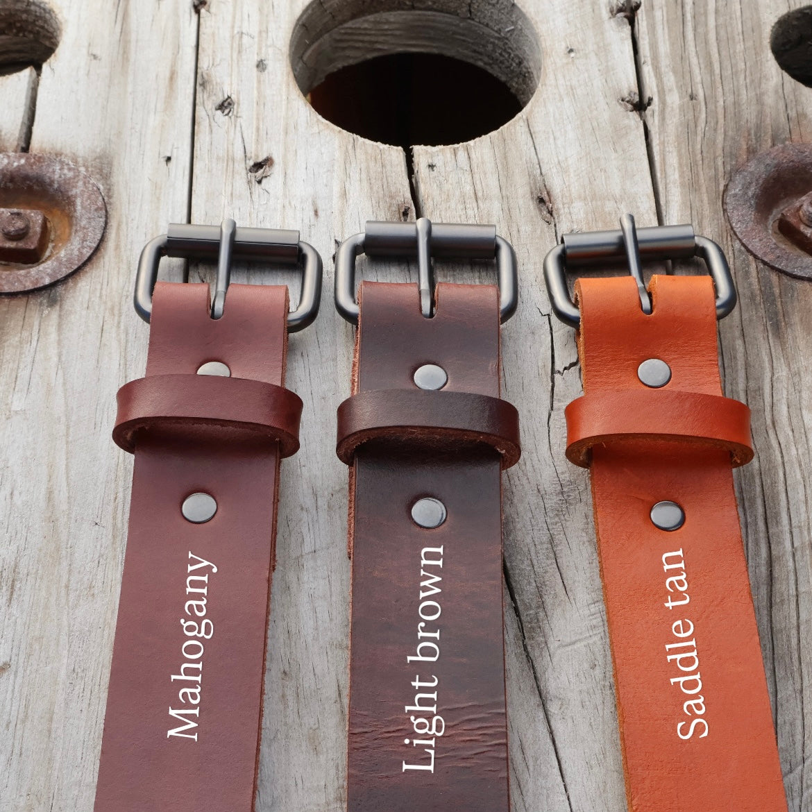 Three leather belts labeled 'Mahogany', 'Light brown', and 'Saddle tan' on a wooden background.