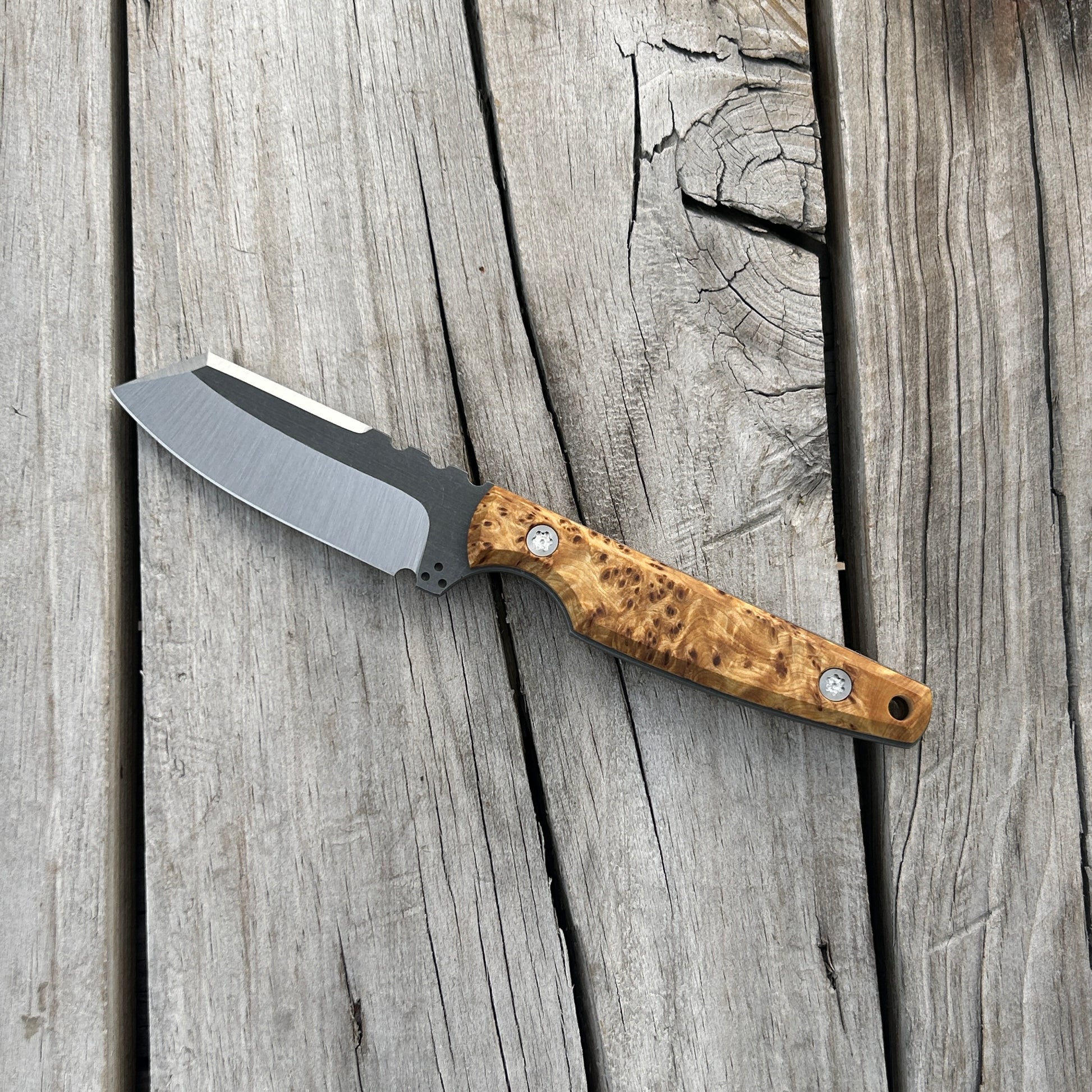 Fixed blade knife with yellow cedar burl handle sitting on wooden surface 