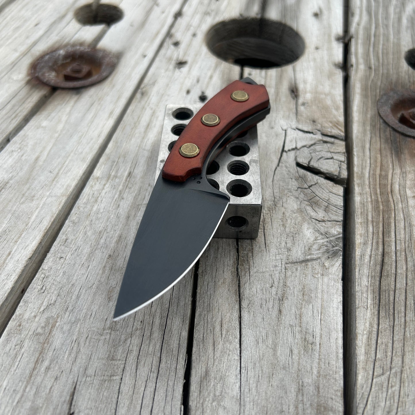 Fixed blade knife with leather handle scales sitting on metal block on wood surface 