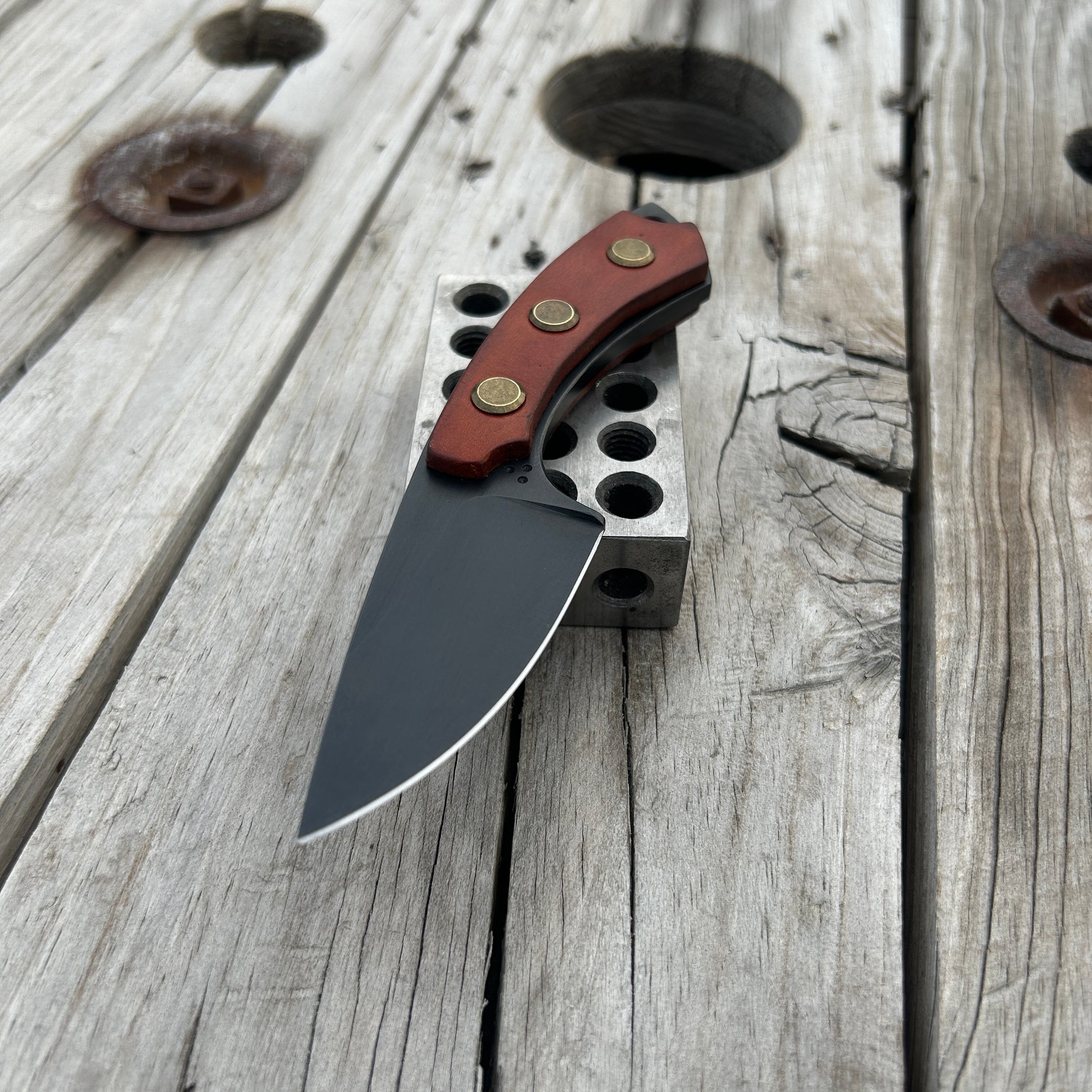 Fixed blade knife with leather handle scales sitting on metal block on wood surface 