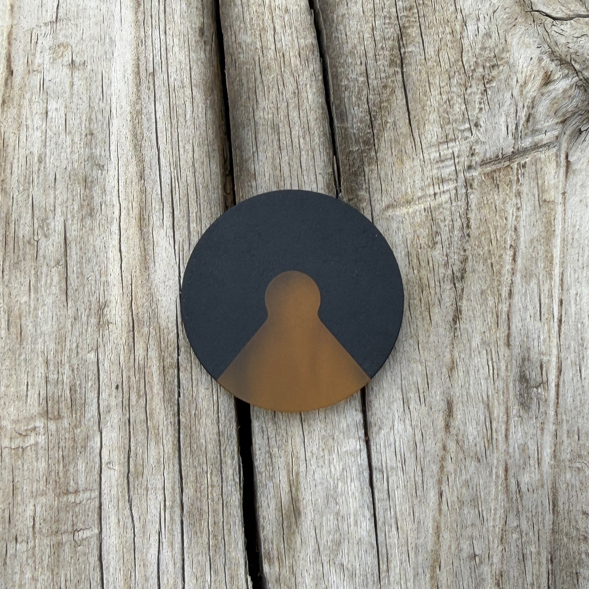 a round black coin with a triangular cutout with a amber colored wedge inlay, laying on wooden surface 