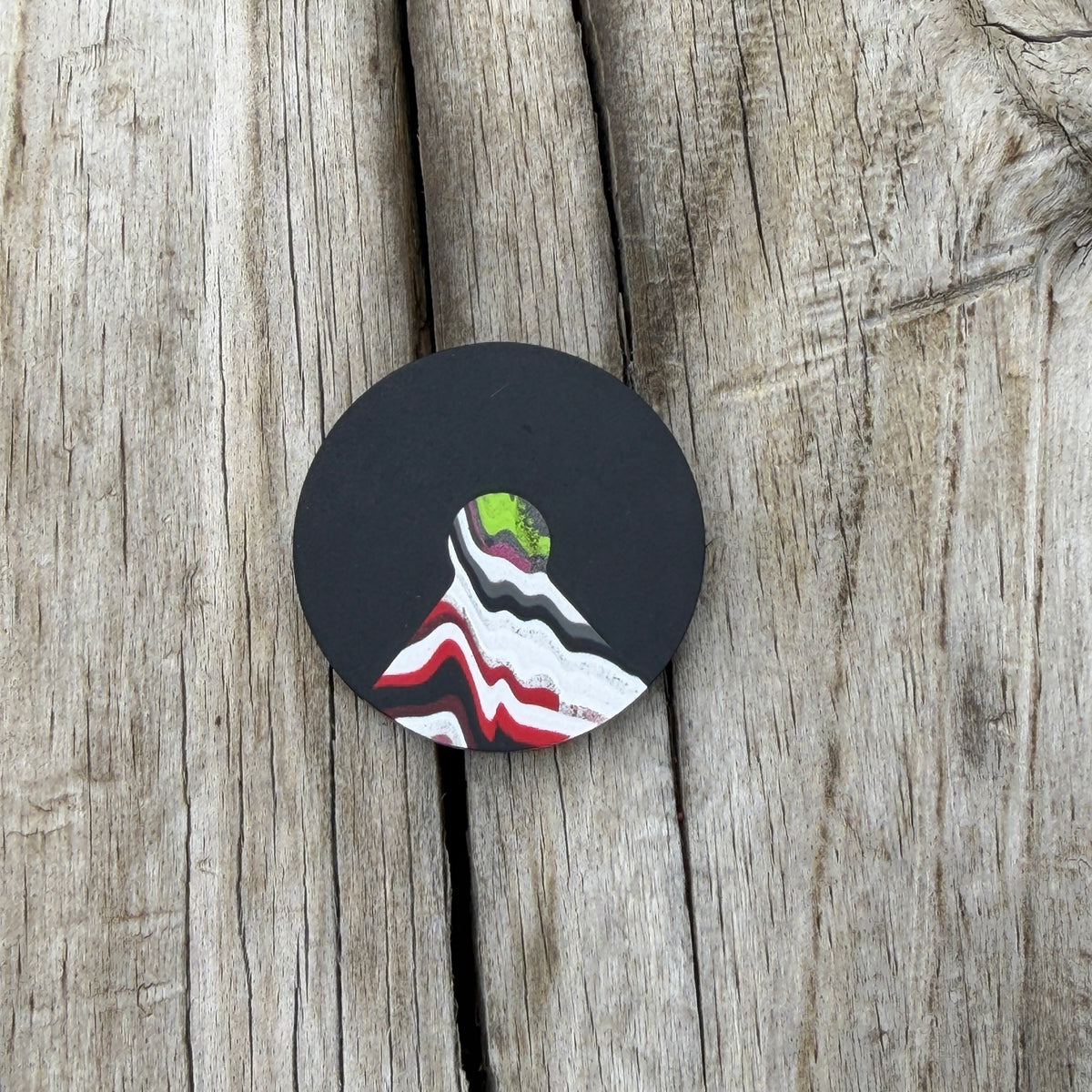 a round black coin with a triangular cutout with a colorful wedge inlay, laying on wooden surface 