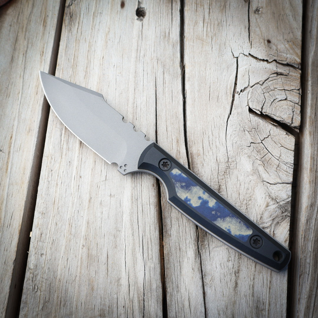 fixed blade knife with blue/green inlay on black handle sitting on wooden surface