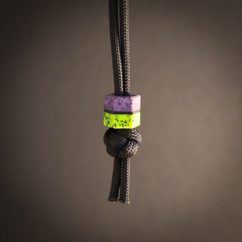Black cord with a purple and green hex bead on a brown background