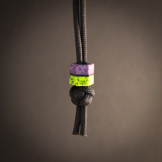 Black cord with a purple and green hex bead on a brown background