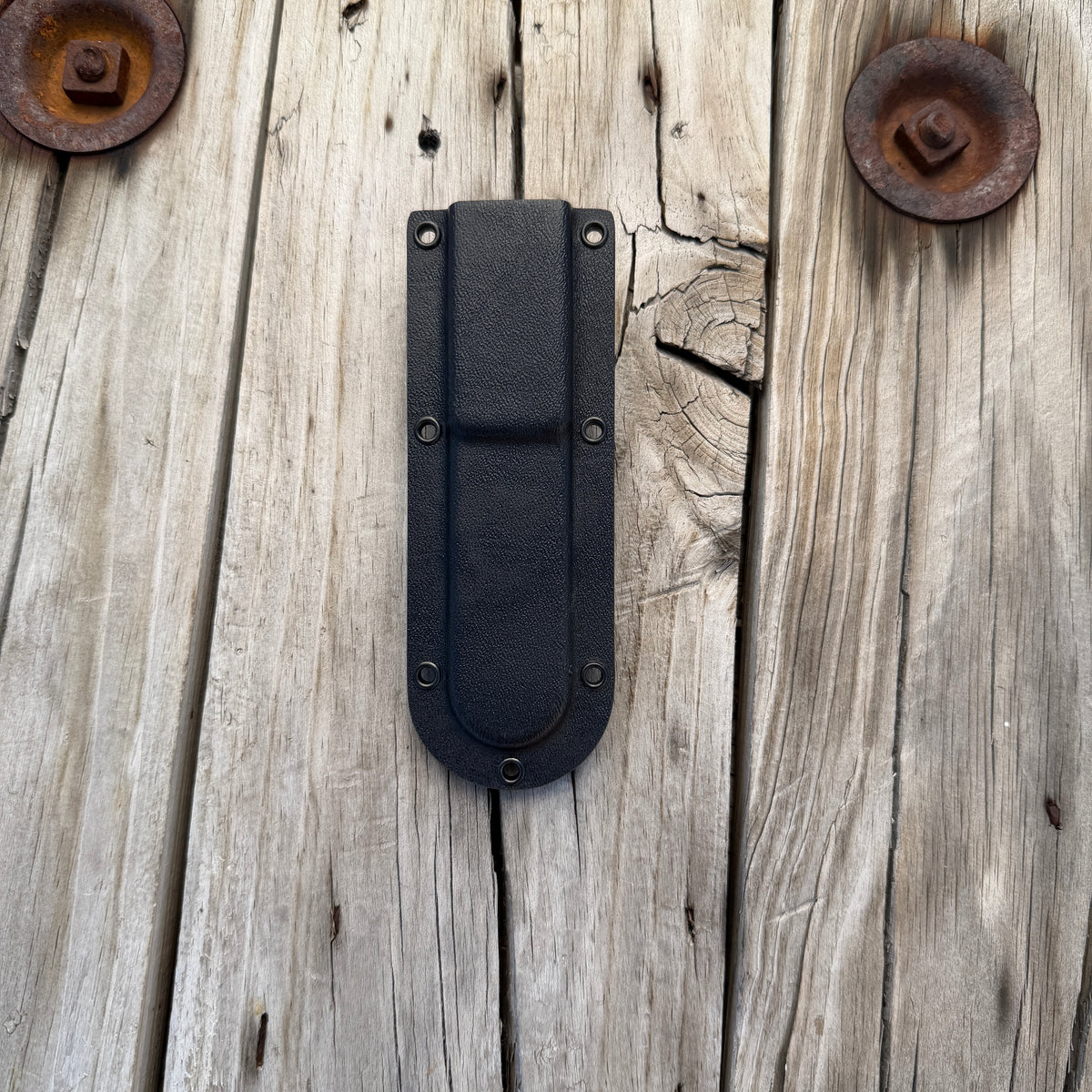 Back side of black kydex deep pocket knife sheath sitting on wooden surface 