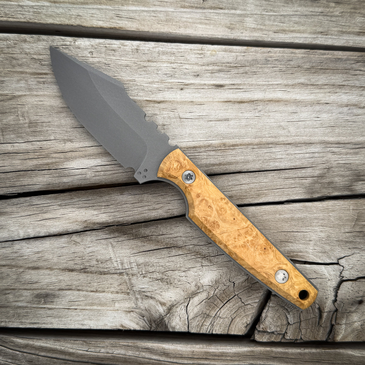 A fixed-blade knife with a matte gray blade and a light tan marbled wooden handle  resting diagonally on weathered gray wooden planks.