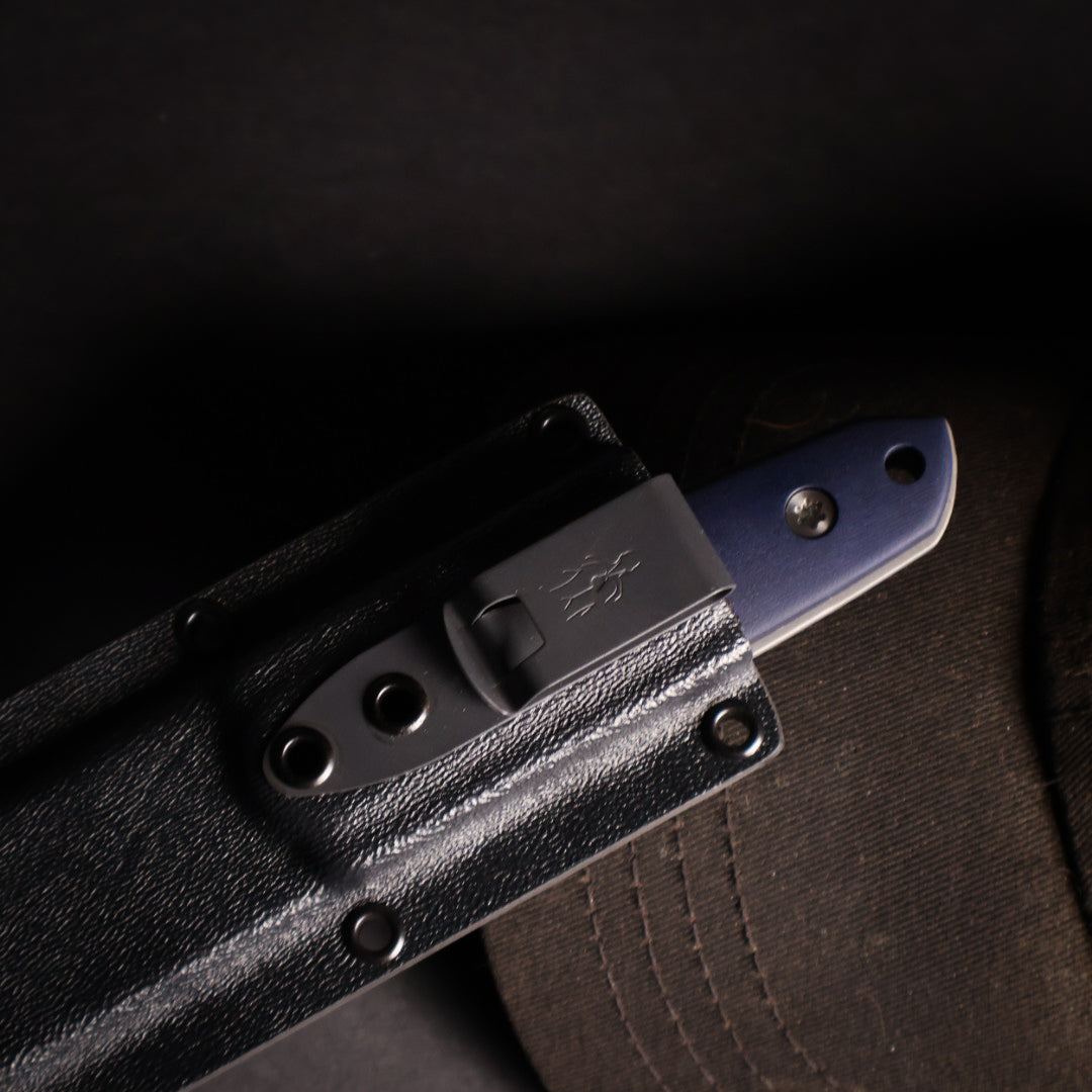 knife in kydex sheath. showing small amount of handle exposed. propped up on a black ballcap bill. 