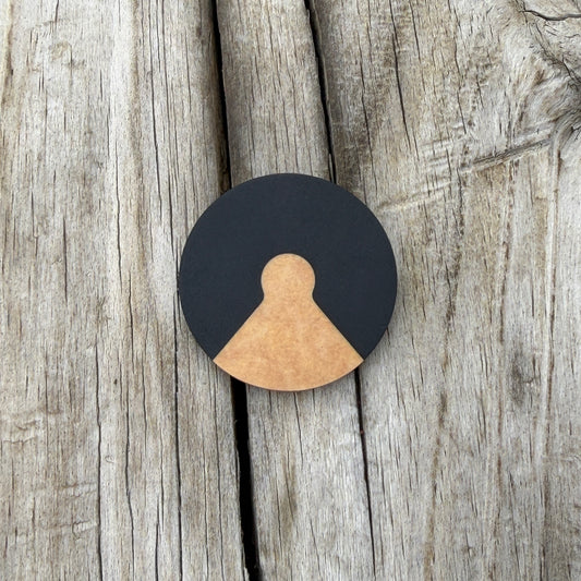 A round black coin with a triangular cutout with a tan inlayed piece, placed on a rustic weathered wood background.