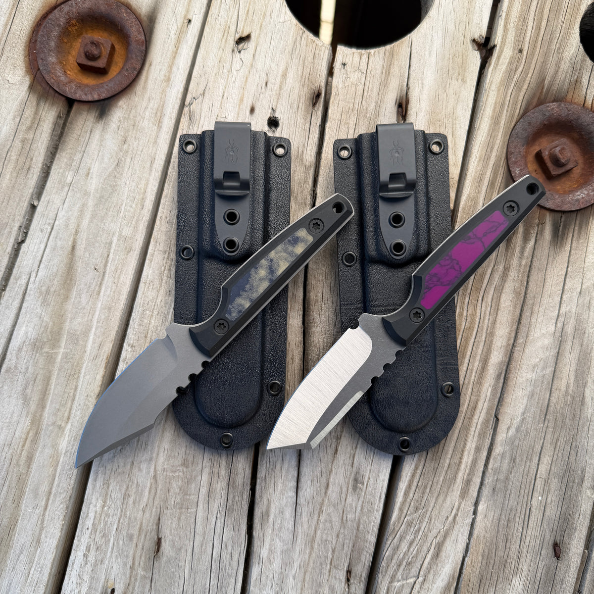 two fixed blade knives sitting on two kydex knife sheaths. All sitting on weathered wooden surface 