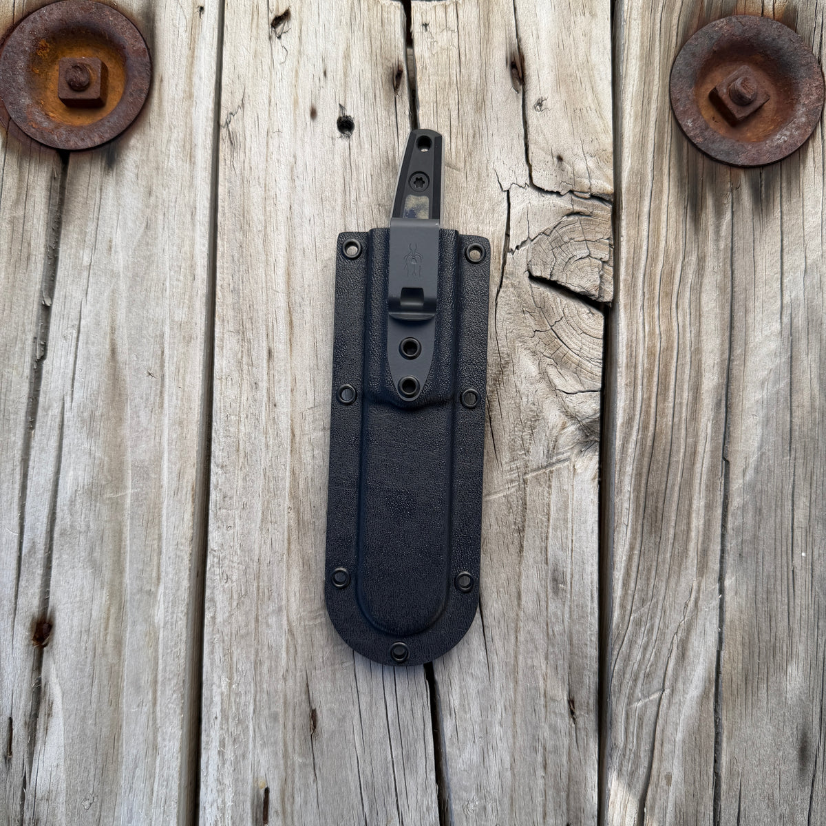 Deep pocket knife sheath with knife handle protruding out the top by approximately an inch and a half. Sitting on wooden surface 