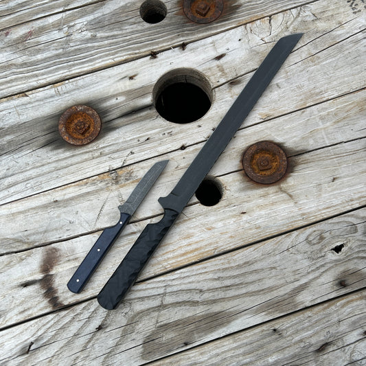 Large skinny tanto style knife/short sword next to small Ghost knife for visual size comparison. Large knife is about 3 times the length of the smaller and double the width