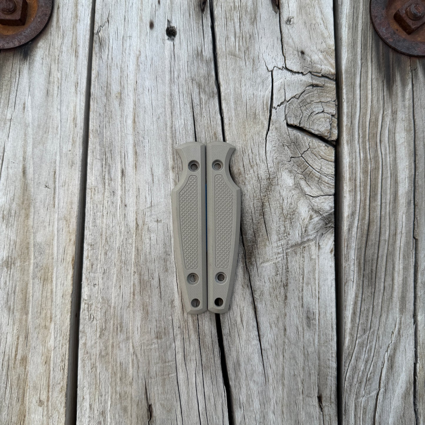 Gray textured knife handle scales sitting on wooden surface 