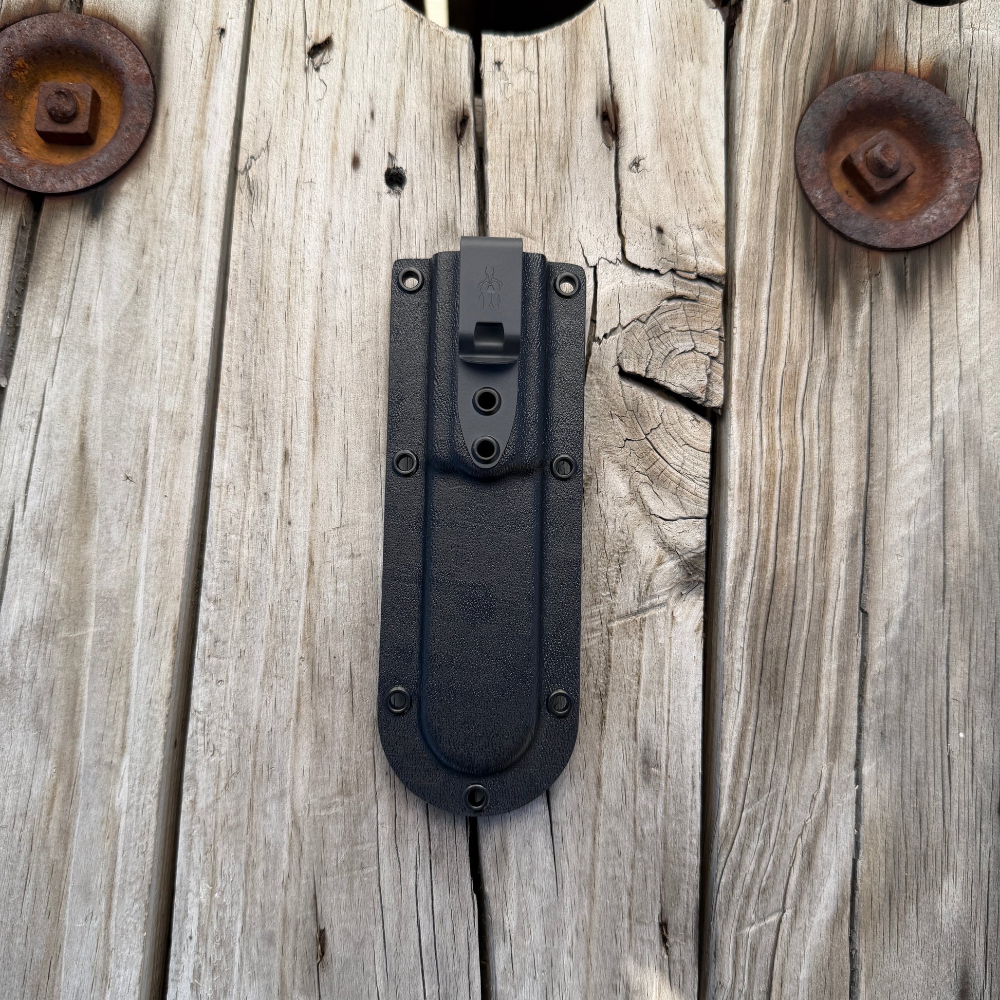 Black deep pocket kydex knife sheath with dark gray clip sitting on wooden surface 