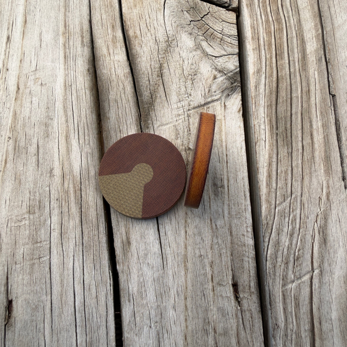 two edc coins sitting on wooden surface. Coins are dark brown with green triangle inlay. One coin is sitting on edge showing the butterscotch interior and dark brown patina outer edges