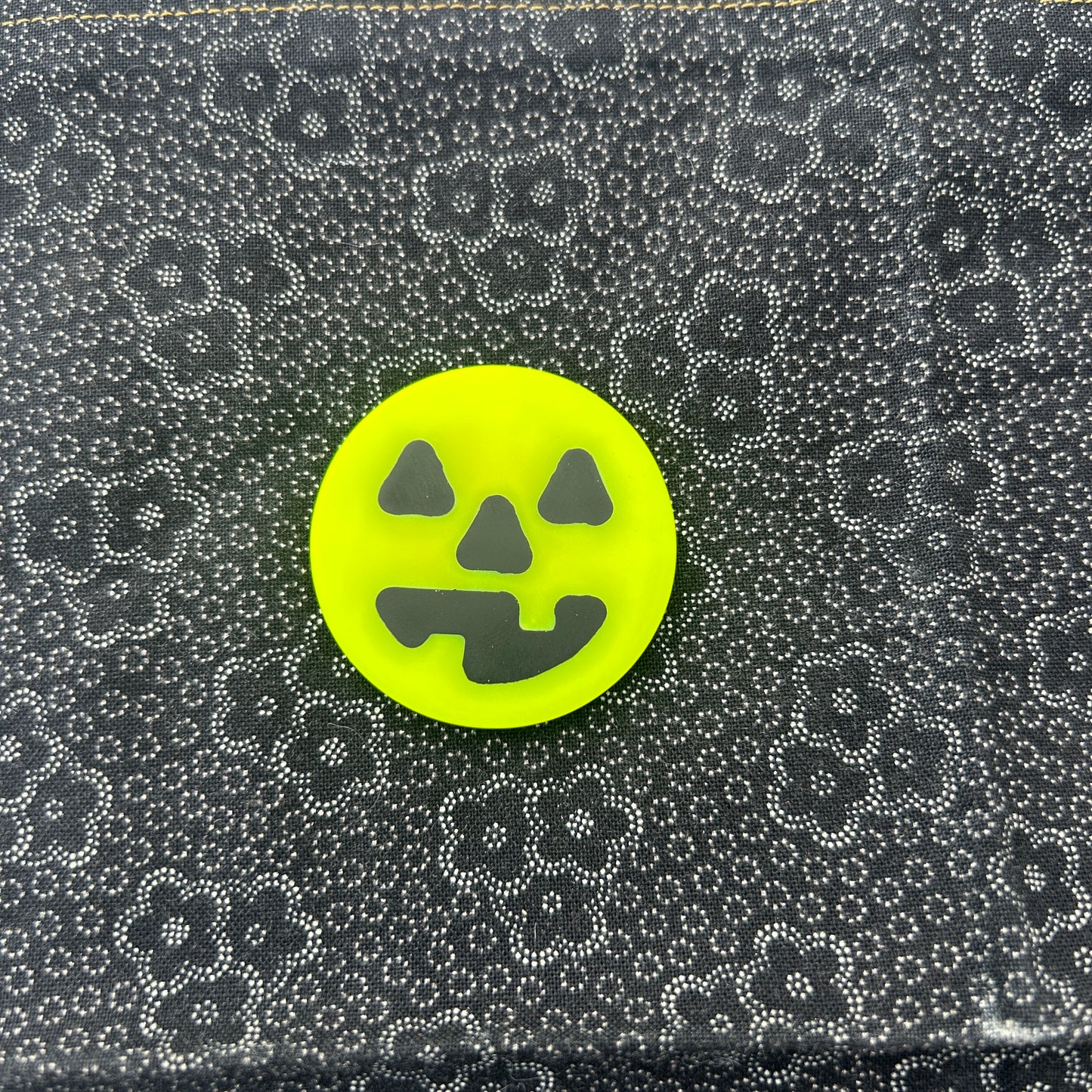 round neon yellow worry coin with happy black jack-o-lantern face in the middle