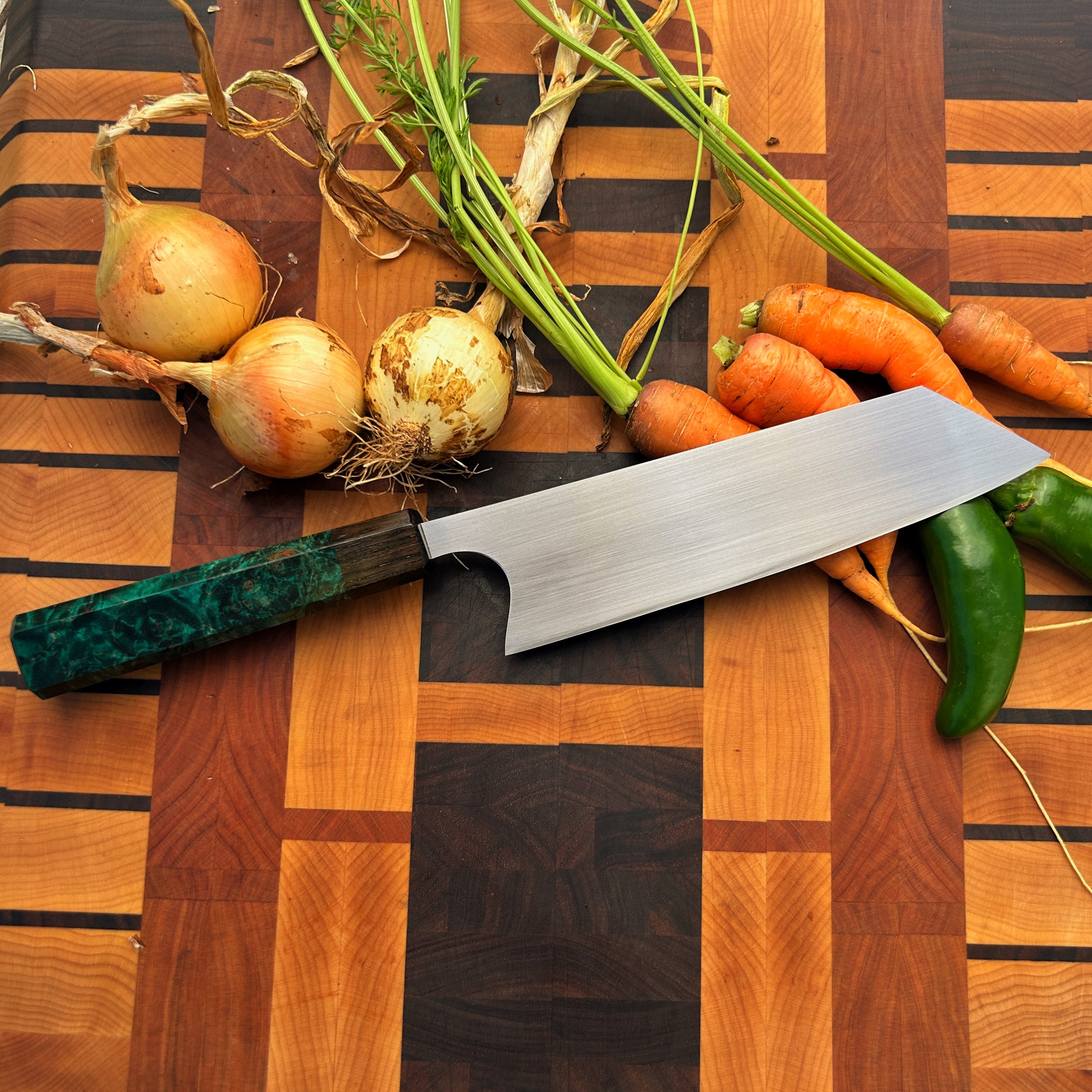 bunka kitchen knife with green handle sitting on cutting board with vegetables