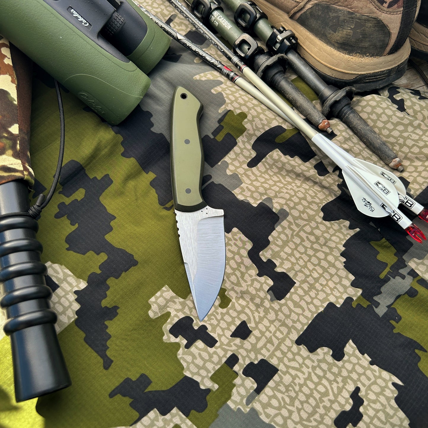 Layered OD green & black handled drop point hunter knife pictured with hunting gear. Great knife for any outdoorsman
