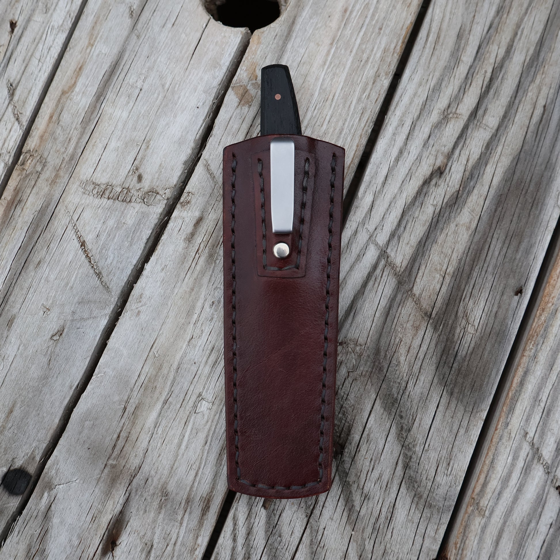 Brown leather knife sheath with a silver clip on a wooden surface